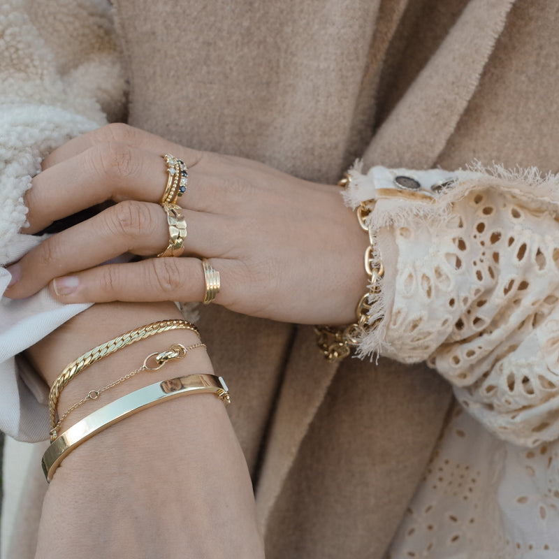 Pols met gouden armbanden van Melanie Pigeaud, waaronder de Snake armband 14k goud met een zilveren kern. En een hand met ringen