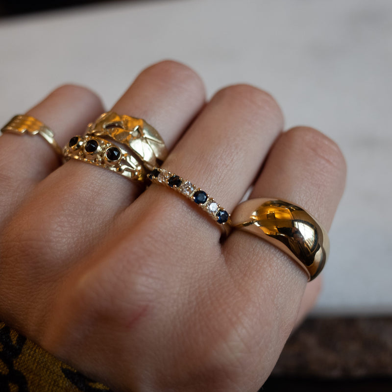 Hand met gouden ringen, waaronder de Melanie Pigeaud saffier zirconia rijring in 14 goud