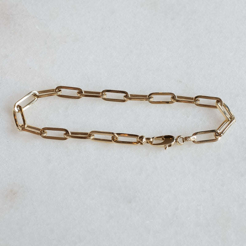 Drawn chain armband in 14k goud door Melanie Pigeaud gepresenteerd op marmeren steen.