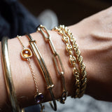 Pols met vijf gouden armbanden van Melanie Pigeaud, waaronder de getekende chain armband in 14K goud.  
